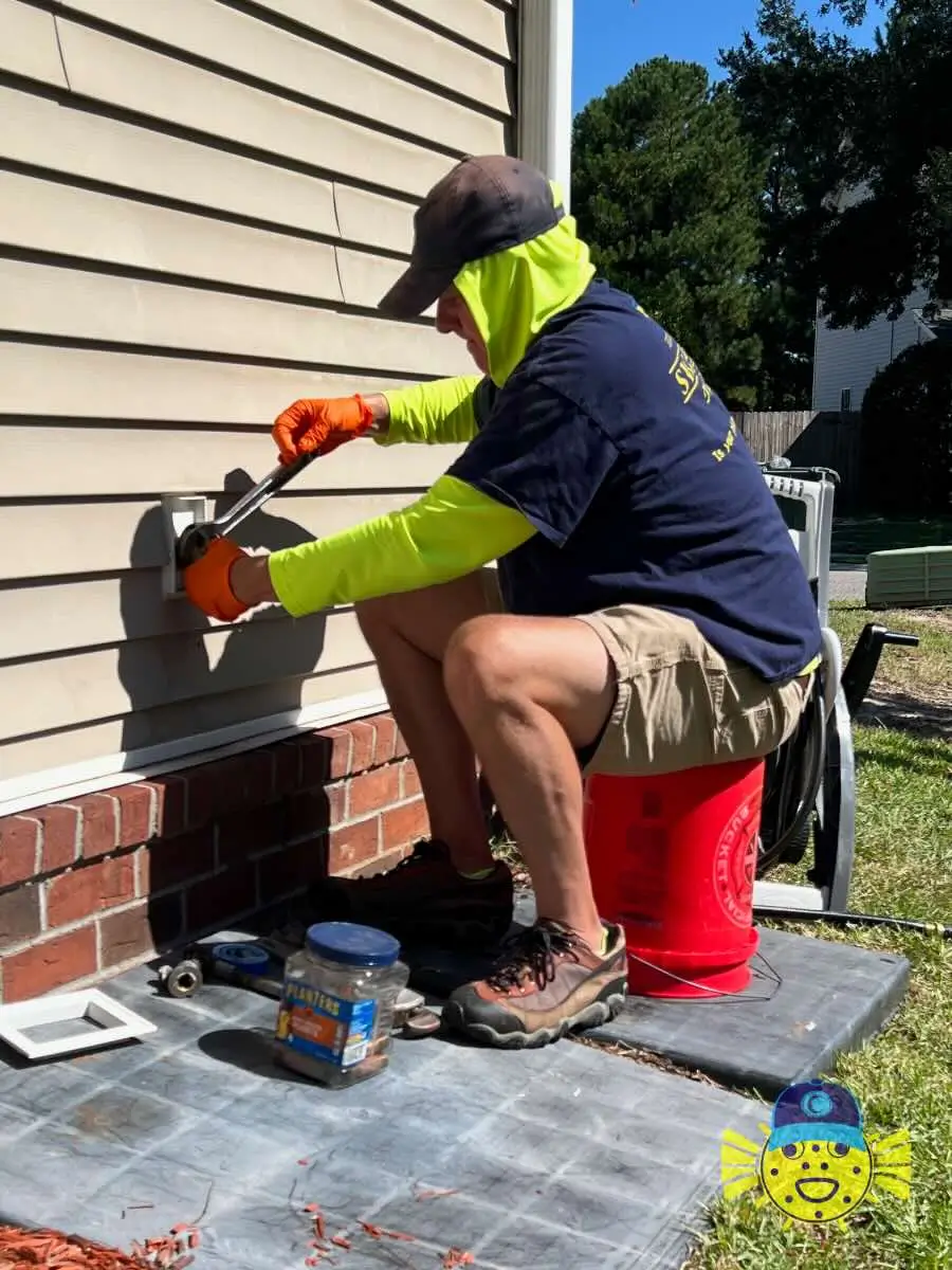 Swell Guy Plumbing technician using a wrench to replace an outdoor hose bib on a residential vinyl siding home in Hanahan, SC.