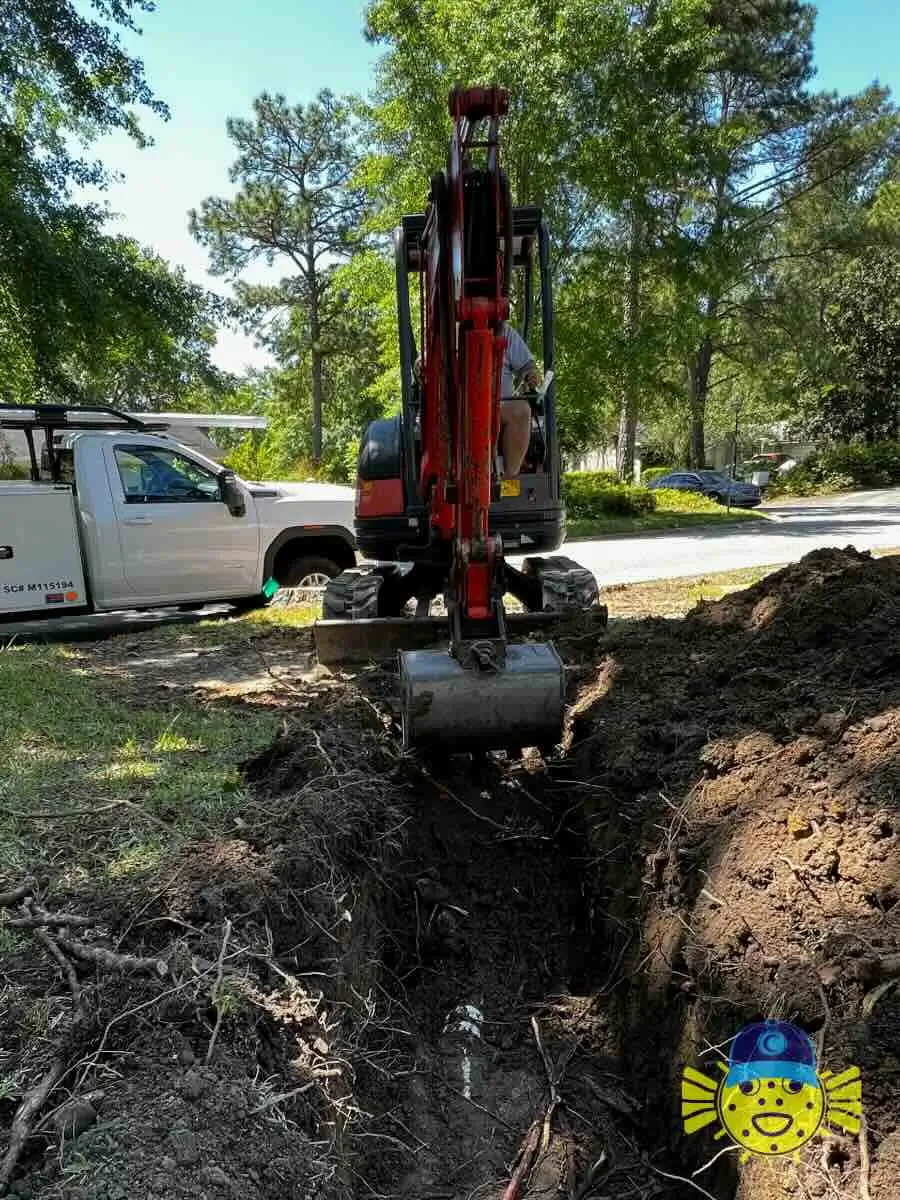 Red excavator digging a trench for a sewer line replacement in Hanahan, SC by Swell Guy Plumbing.