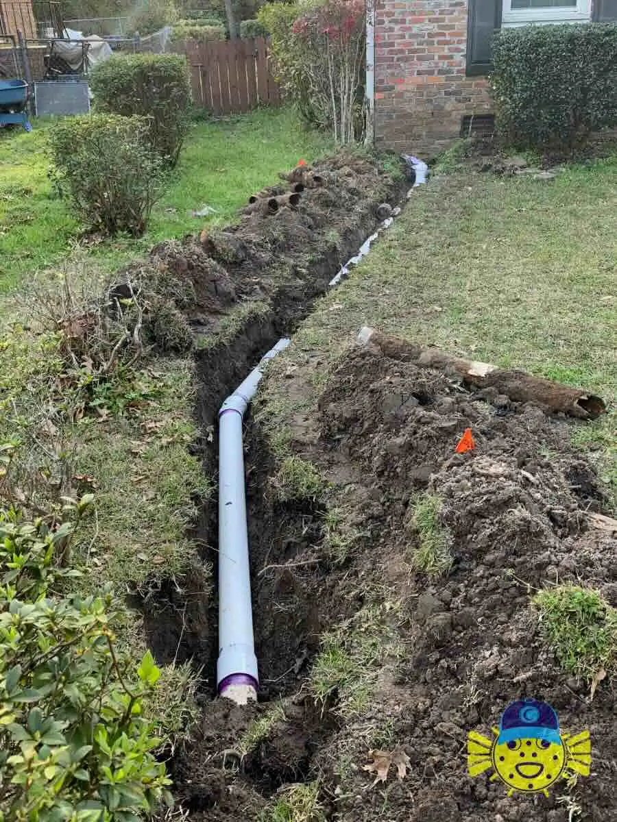 Newly installed white PVC sewer pipe in a freshly dug trench outside a residential home in Hanahan, SC, by Swell Guy Plumbing.